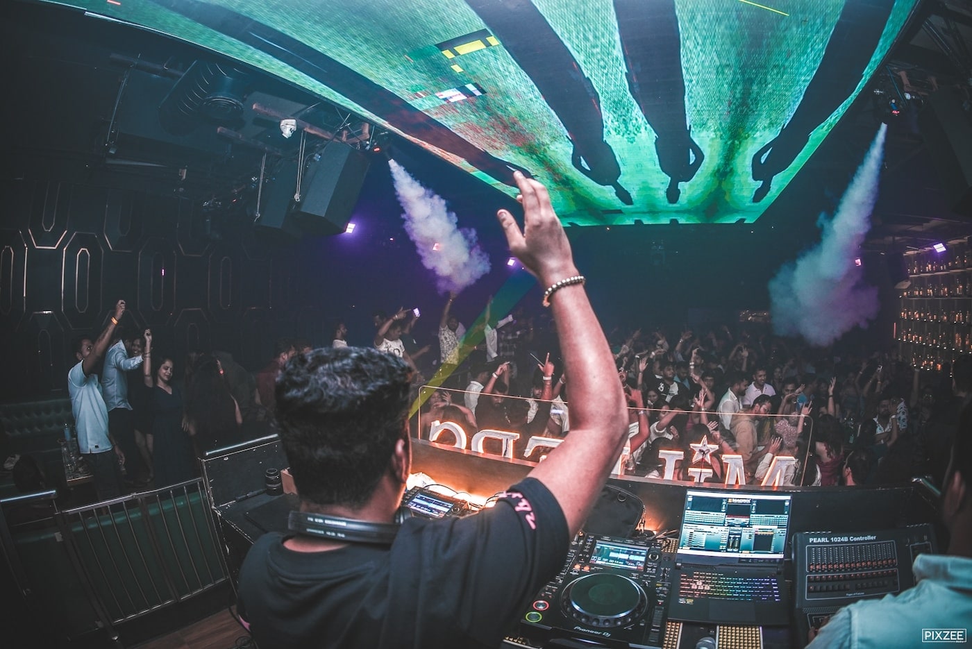 A performer facing a crowd under stage lighting at a late-night event.