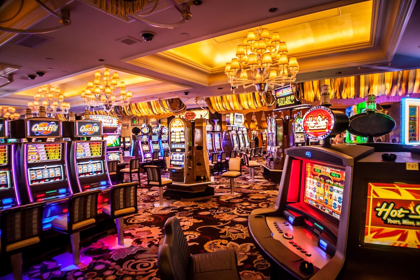 Rows of illuminated gaming machines with seats along a patterned floor.