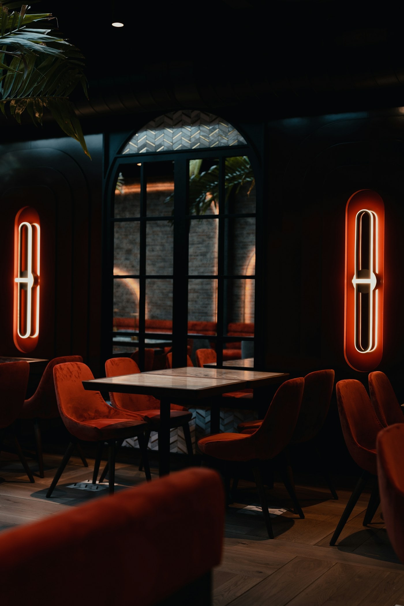 A dark dining room with warm neon accents and upholstered seating.